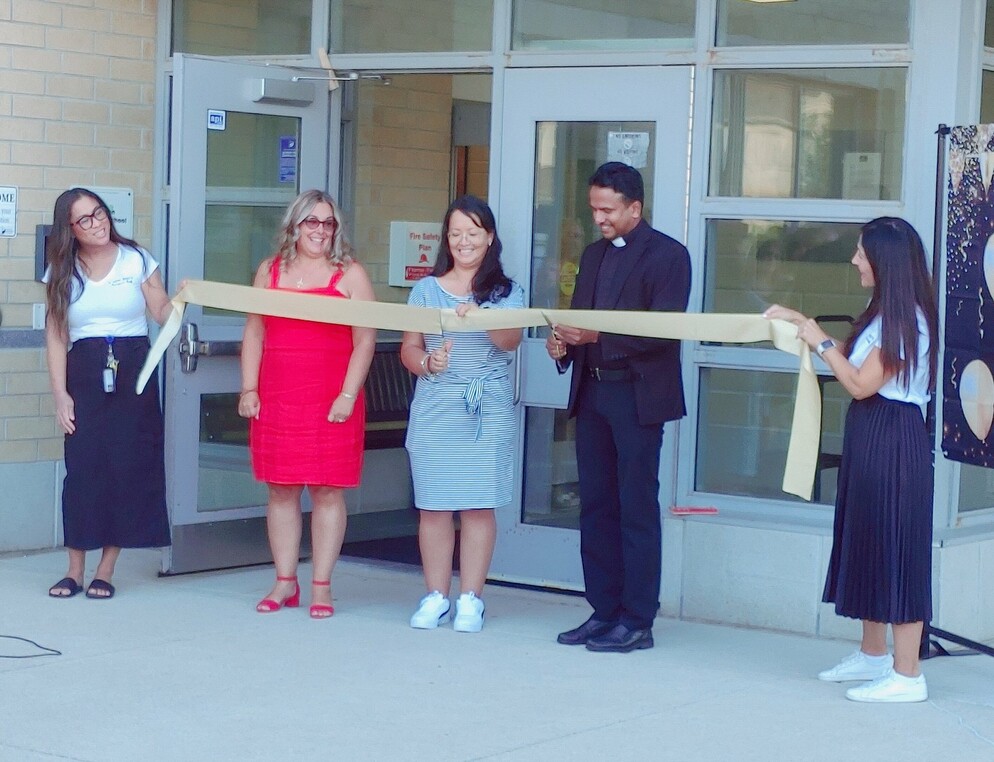 People cutting a ribbon in front of a school